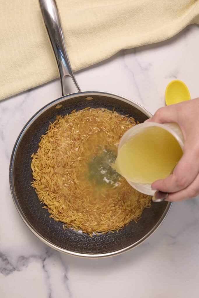 adding chicken stock to the toasted orzo