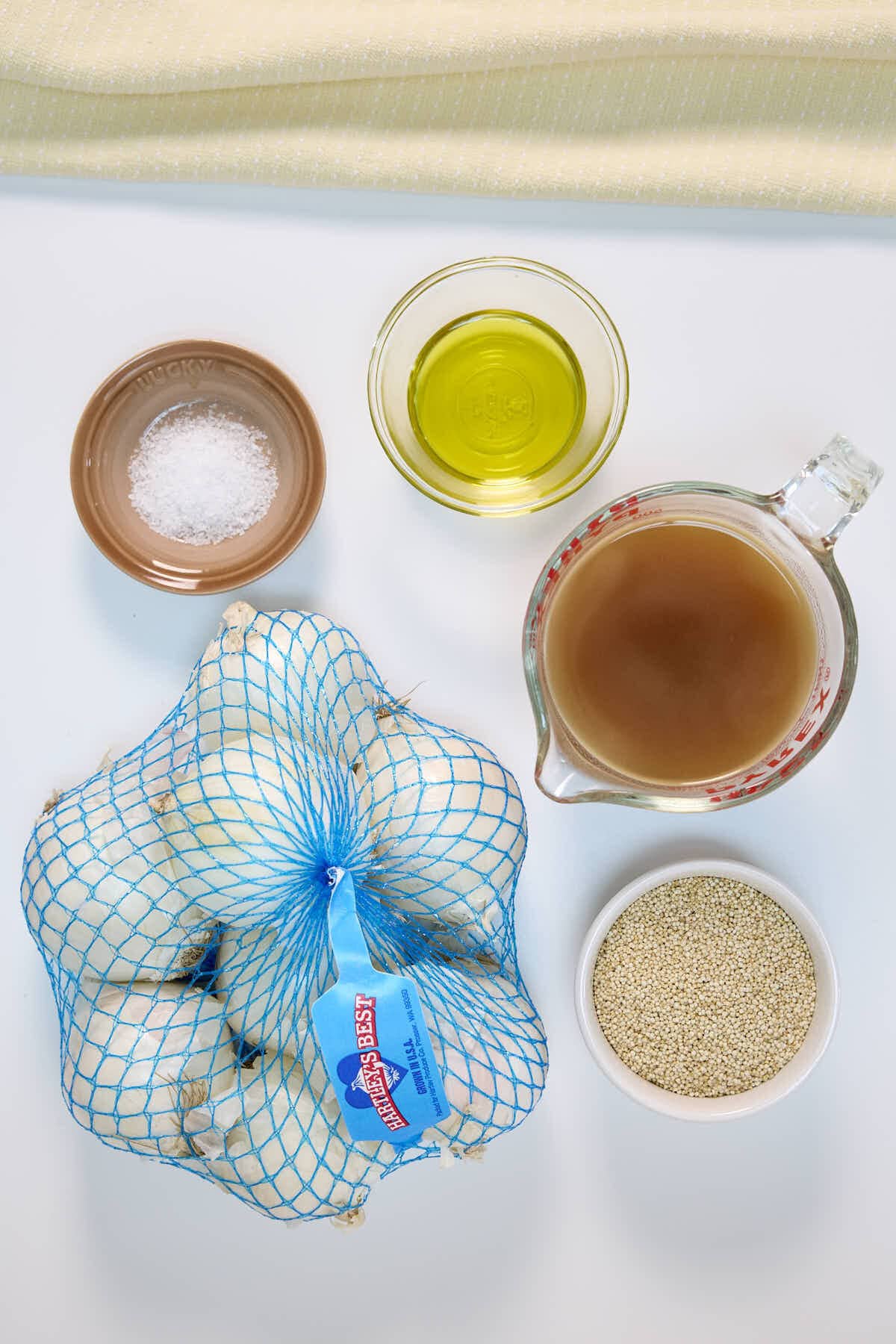 ingredients for the French onion quinoa recipe; a bag of onions, salt, olive oil, beef stock, and quinoa