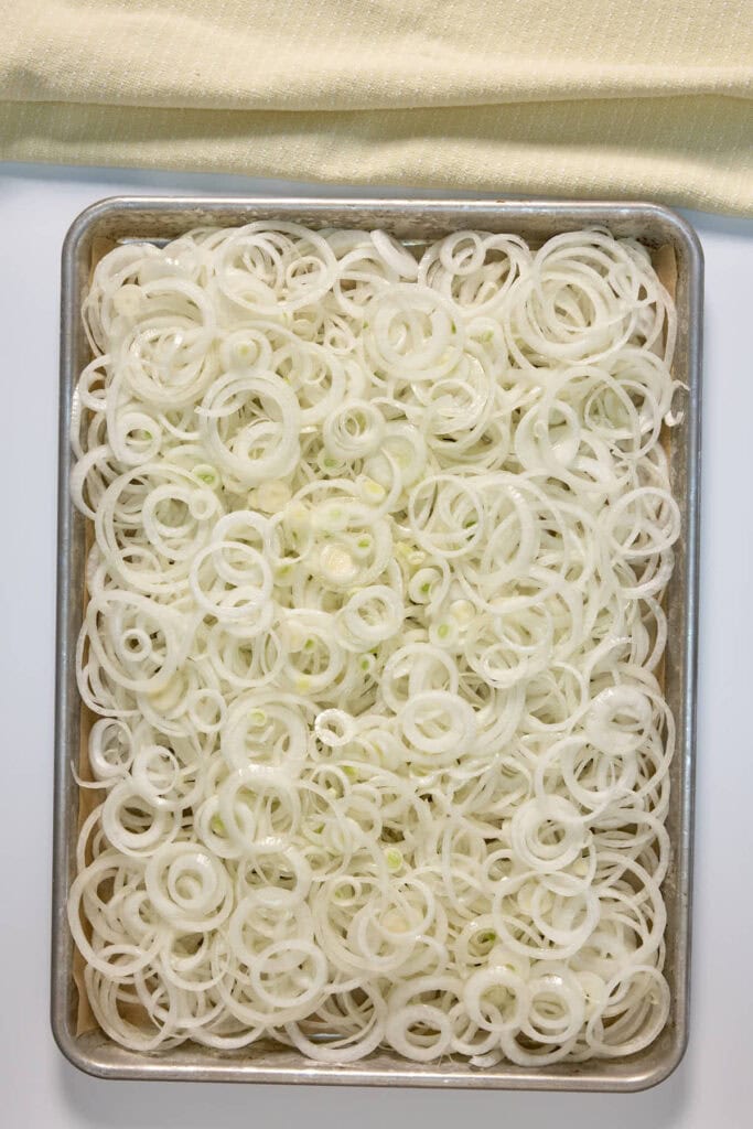 sliced onions spread out on a sheet pan to be baked and carmelized