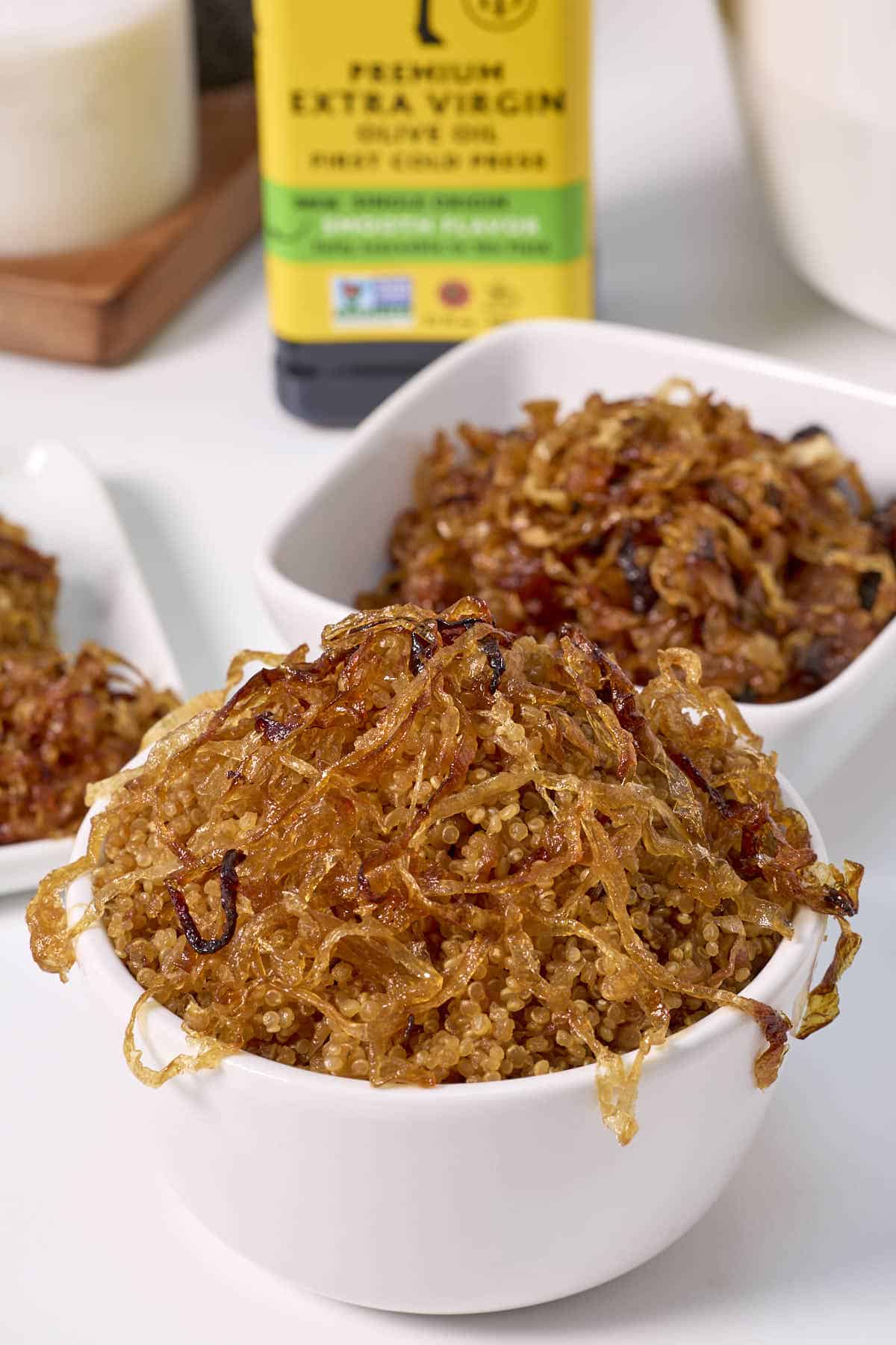 French onion quinoa in a bowl with carmelized onions spilling over the dish and in a bowl in the background