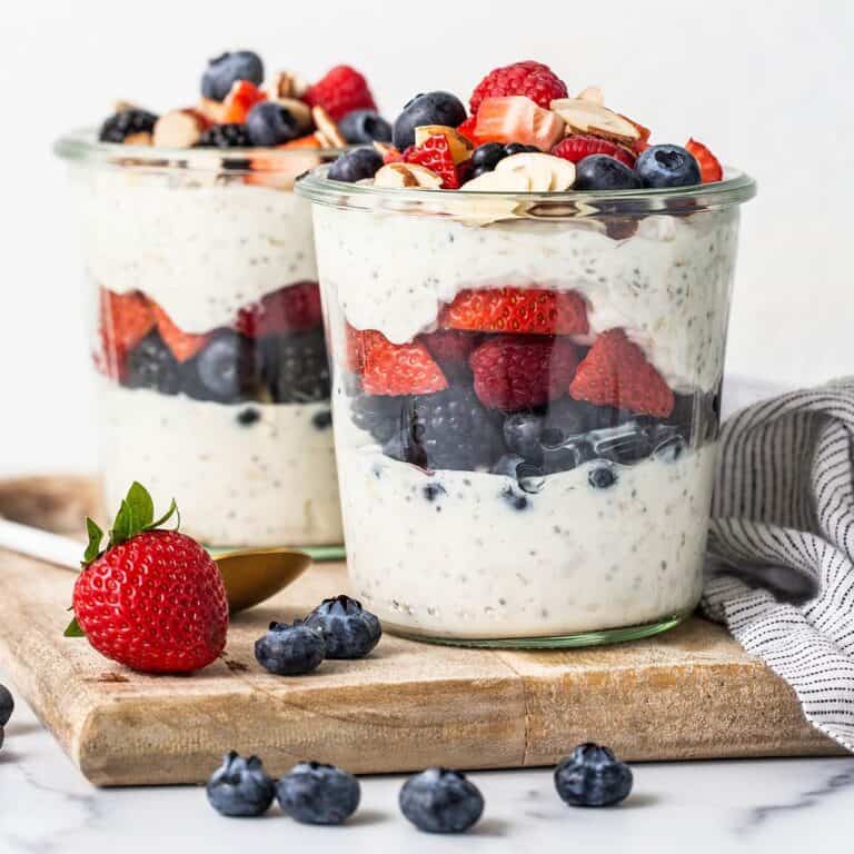 Cups of high protein overnight oats on a wood serving board surrounded by berries