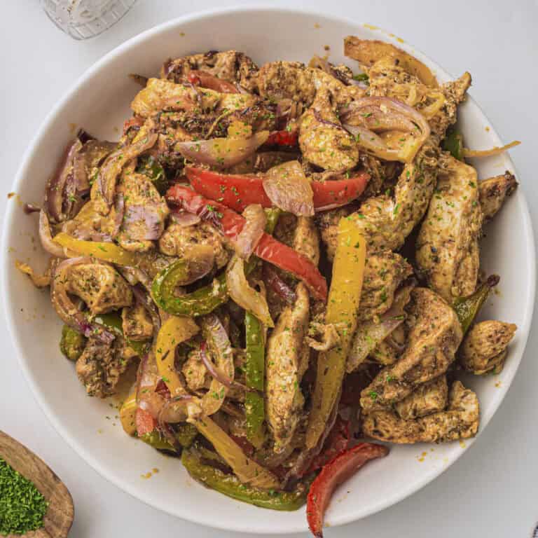 Air fryer chicken fajitas from this recipe served on a plate with some chopped cilantro in the bottom corner in a dish