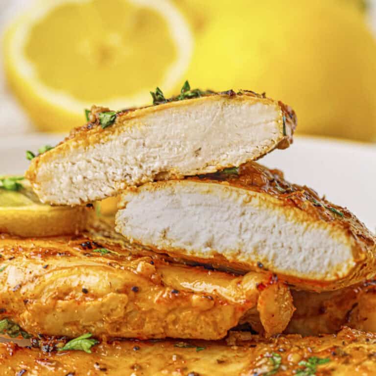 Baked lemon chicken breast on a plate, with one sliced so you can see the tender and juicy inside