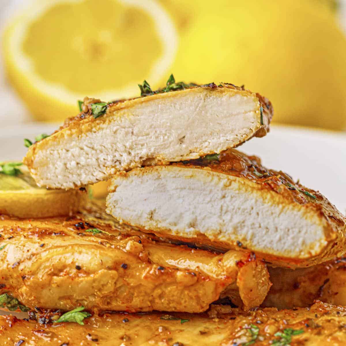 Baked lemon chicken breast on a plate, with one sliced so you can see the tender and juicy inside