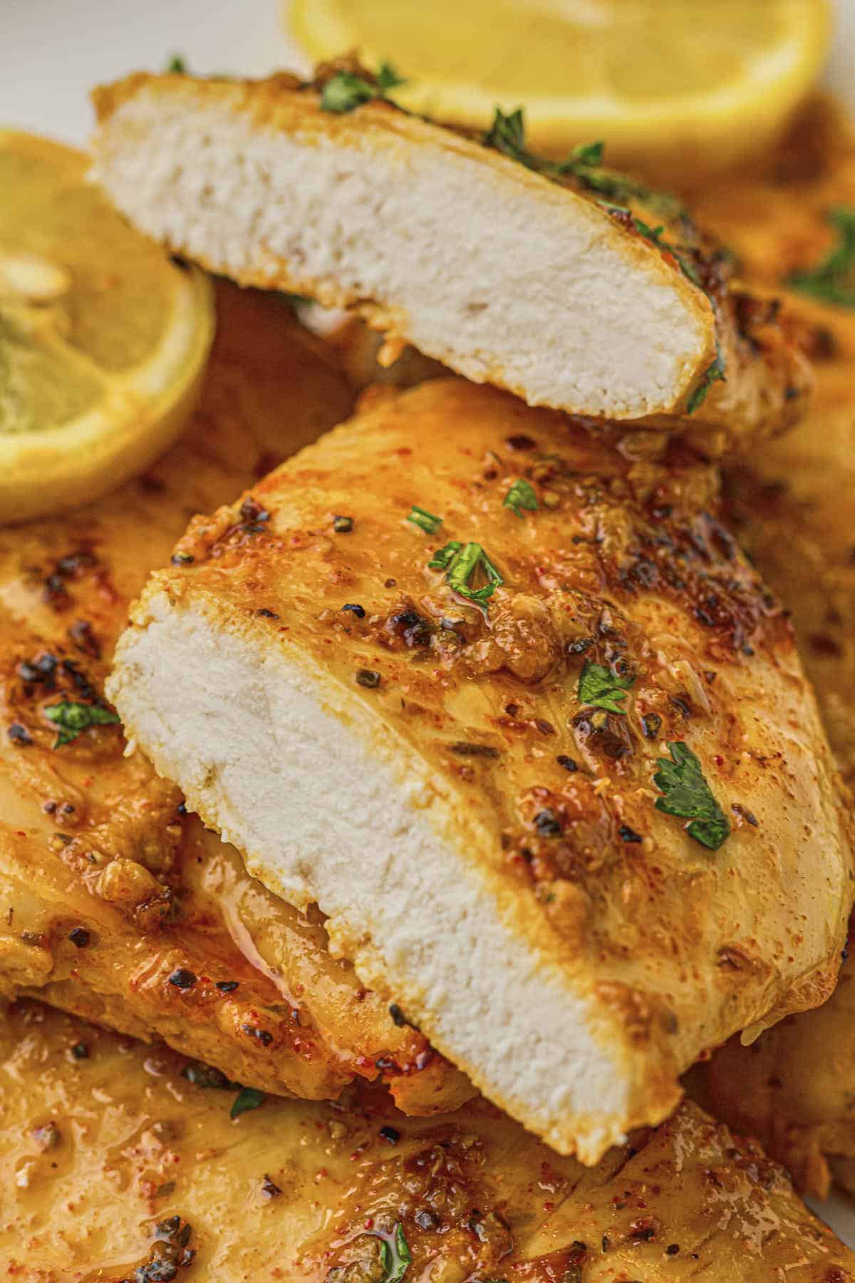 Hero shot of the baked lemon chicken breast served on a plate with one sliced to reveal the tender and juicy meat