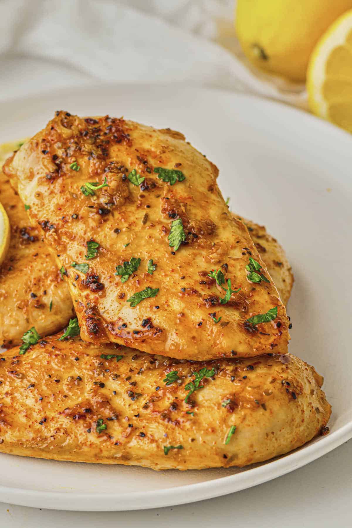 Baked lemon chicken breast served on a plate with lemon in the background