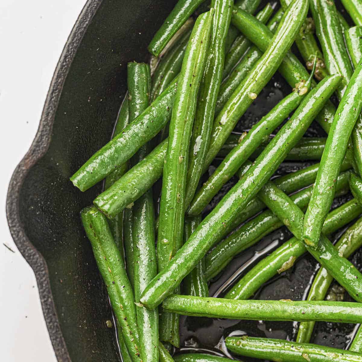 Garlic butter green beans from this recipe being seared in a cast iron pan