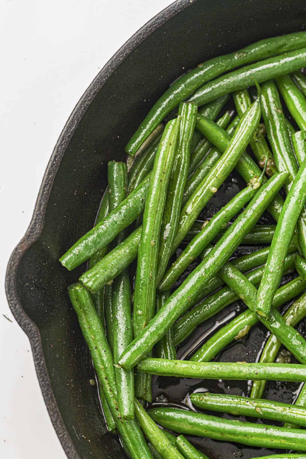 Garlic butter green beans from this recipe in a cast iron pan, full height shot