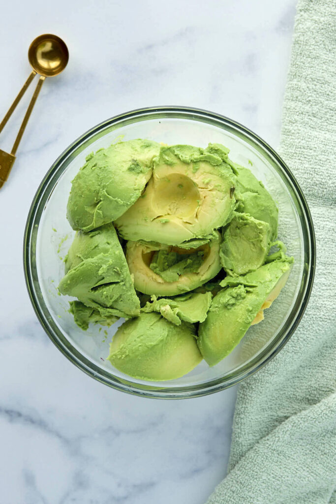 Halved avocado in a bowl ready to be smashed