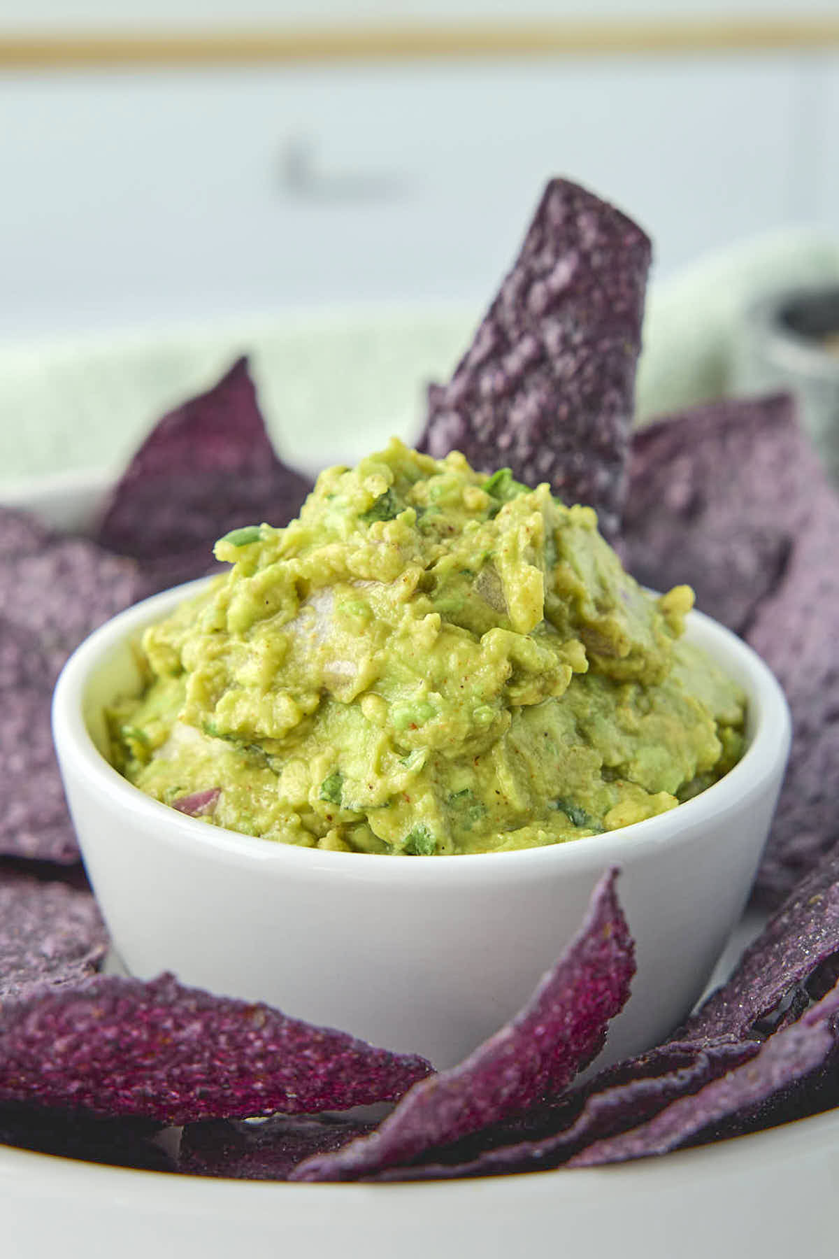 Tall photo of the keto guacamole from this recipe surrounded by some organic blue corn tortilla chips