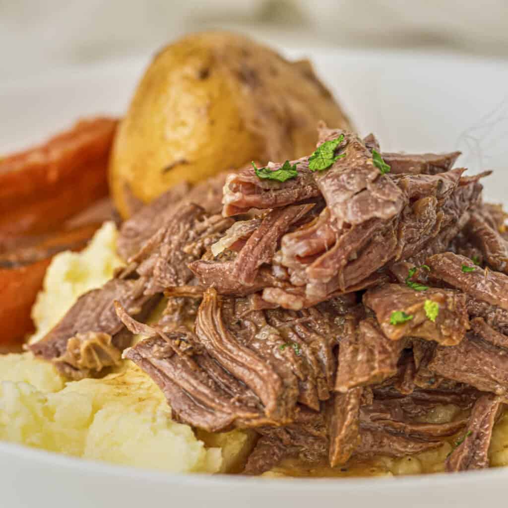 Keto pot roast from this recipe with plated on cauliflower puree with roast vegetables in the background