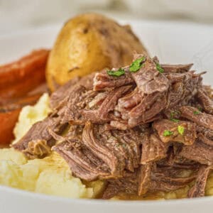 Keto pot roast from this recipe with plated on cauliflower puree with roast vegetables in the background
