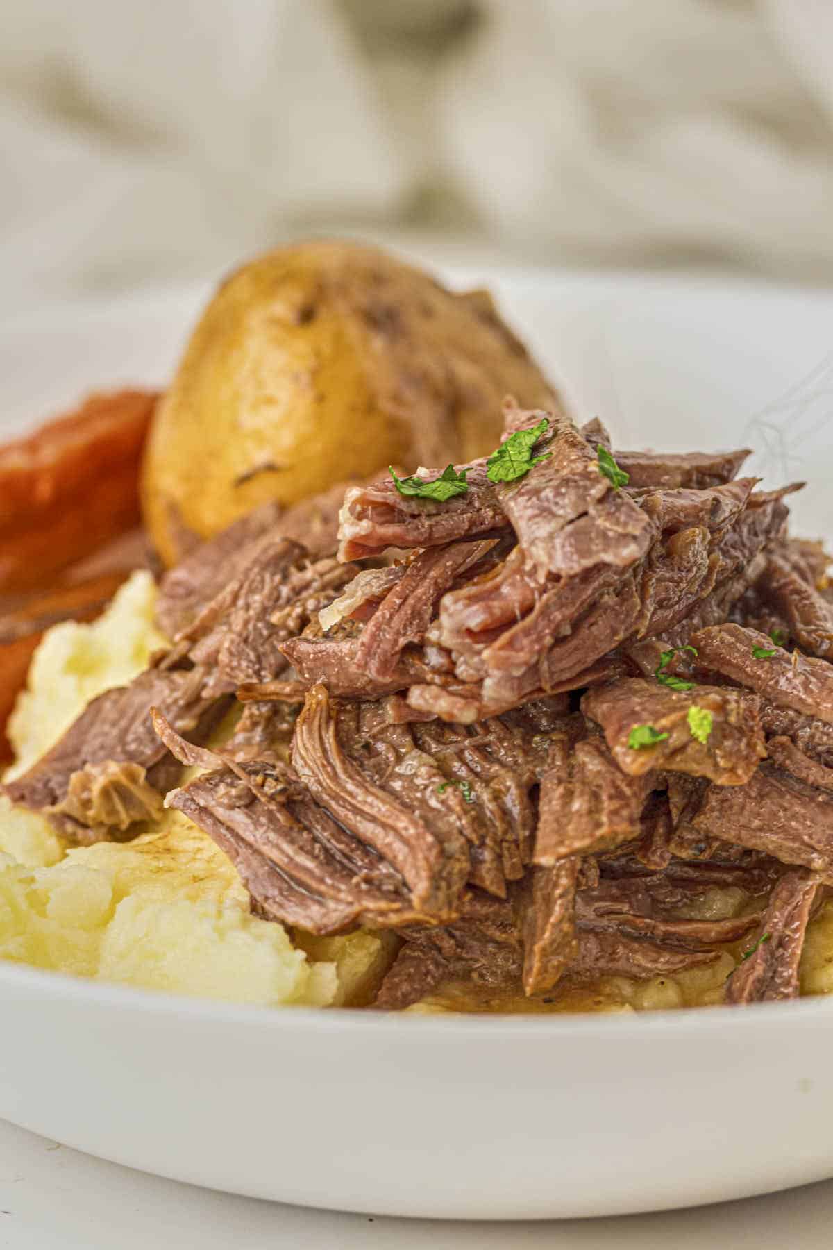 Tall picture of the keto pot roast from this recipe with plated on cauliflower puree with roast vegetables in the background