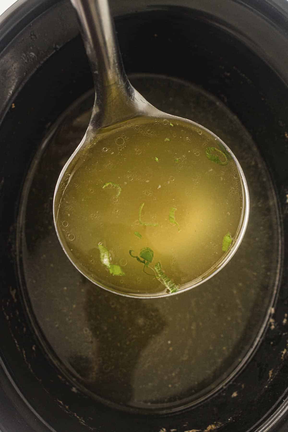 Ladle of slow cooker chicken stock with some green onion