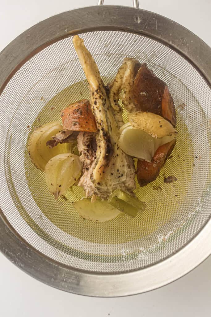 Mesh strainer being used to seperate the solids from the chicken stock