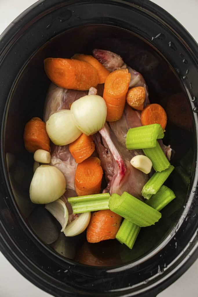 Process photo showing the cut vegetables and garlic added to the slow cooker pot