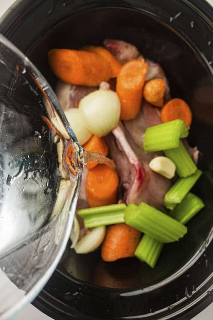 Process photo showing water being poured into the slow cooker pot to cover the chicken and vegetables