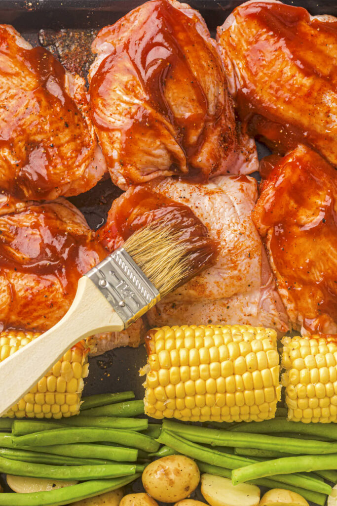 Brushing the baked BBQ chicken thighs with the sauce