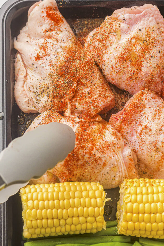 Tongs in the picture with the seasoned chicken thighs